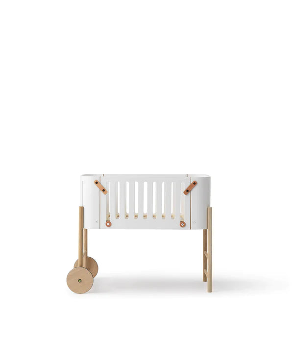 Oliver Furniture witte en eikenhouten co-sleeper naast een volwassen bed, omgezet naar een kinderbankje in een huiselijke setting.