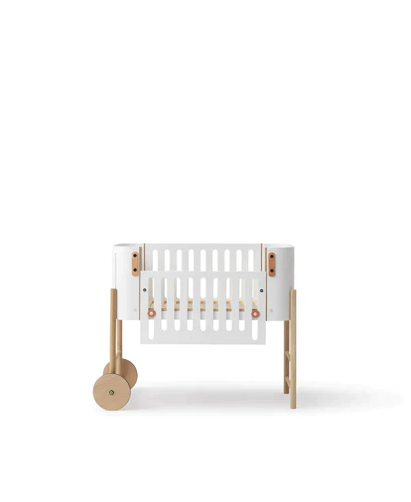 Oliver Furniture witte en eikenhouten co-sleeper naast een volwassen bed, omgezet naar een kinderbankje in een huiselijke setting.
