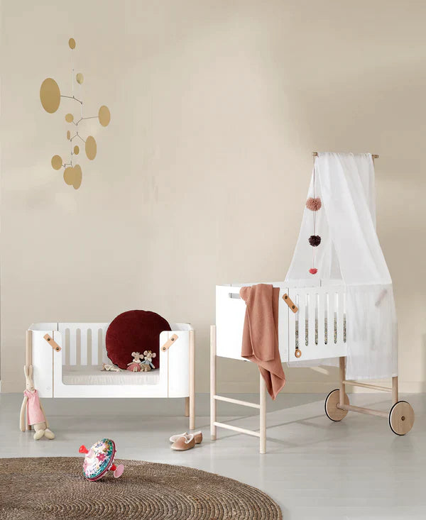 Oliver Furniture witte en eikenhouten co-sleeper naast een volwassen bed, omgezet naar een kinderbankje in een huiselijke setting.