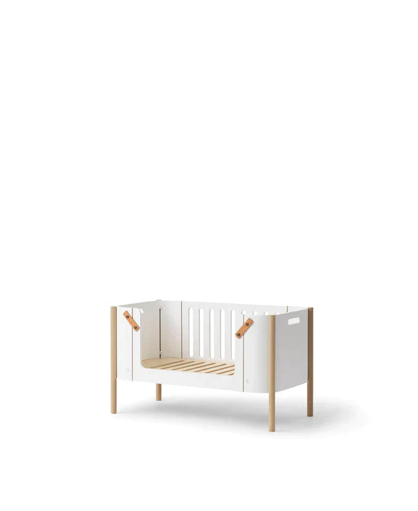 Oliver Furniture witte en eikenhouten co-sleeper naast een volwassen bed, omgezet naar een kinderbankje in een huiselijke setting.