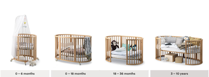 Stokke Sleepi™ Mini V3 wieg in natuurlijke houtafwerking, met zachte ovale vorm en vergrendelbare zwenkwielen.