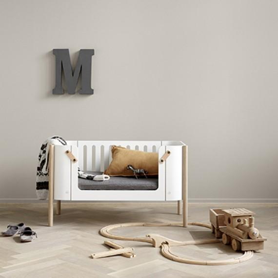 Oliver Furniture witte en eikenhouten co-sleeper naast een volwassen bed, omgezet naar een kinderbankje in een huiselijke setting.
