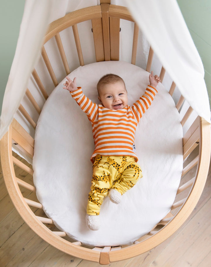 Stokke Sleepi™ Mini V3 wieg in natuurlijke houtafwerking, met zachte ovale vorm en vergrendelbare zwenkwielen.