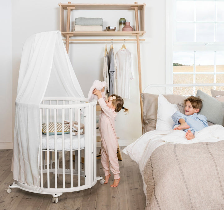 Stokke Sleepi™ Mini V3 wieg in wit, met zachte ovale vorm en vergrendelbare zwenkwielen.