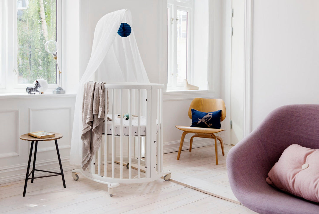 Stokke Sleepi™ Mini V3 wieg in wit, met zachte ovale vorm en vergrendelbare zwenkwielen.