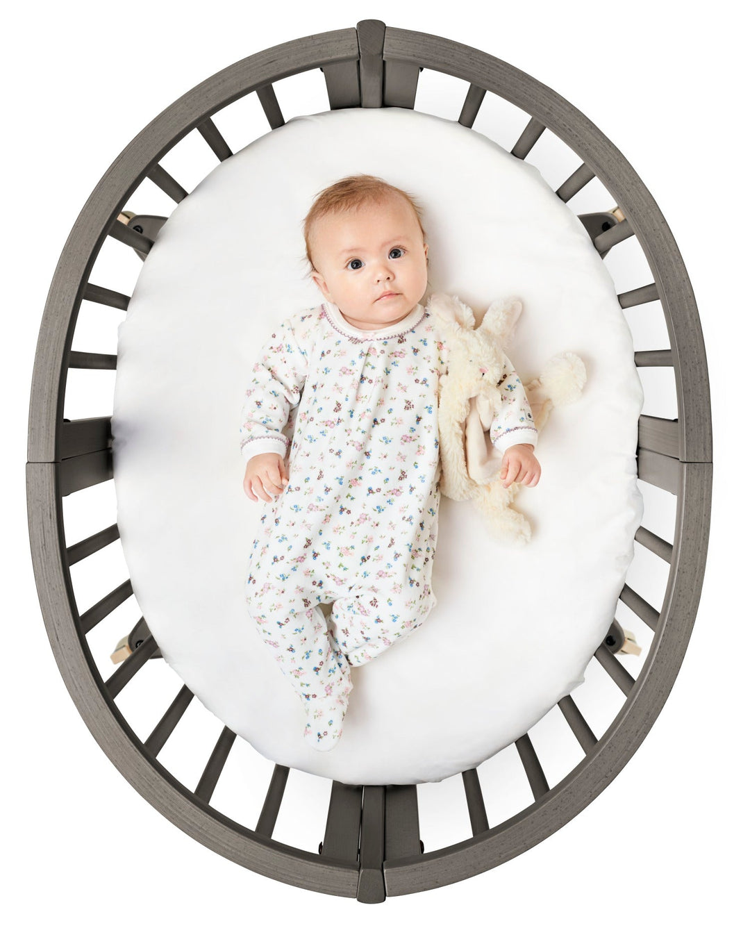 Stokke Sleepi™ Mini V3 wieg in hazy grey afwerking, met zachte ovale vorm en vergrendelbare zwenkwielen.