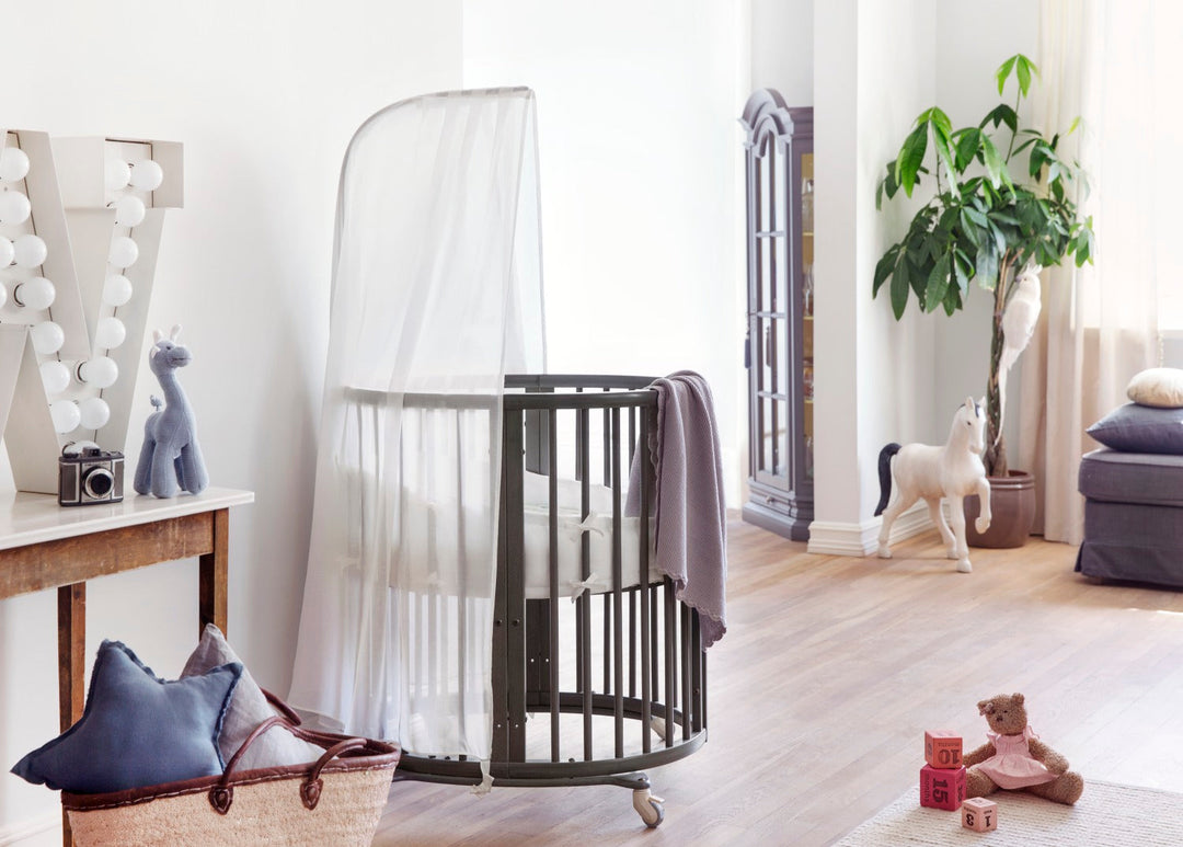 Stokke Sleepi™ Mini V3 wieg in hazy grey afwerking, met zachte ovale vorm en vergrendelbare zwenkwielen.