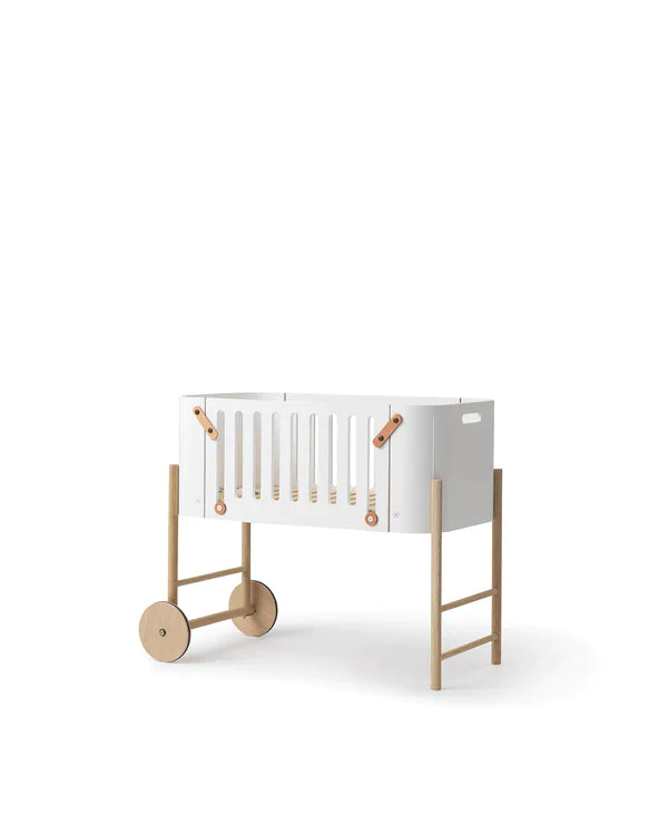 Oliver Furniture witte en eikenhouten co-sleeper naast een volwassen bed, omgezet naar een kinderbankje in een huiselijke setting.