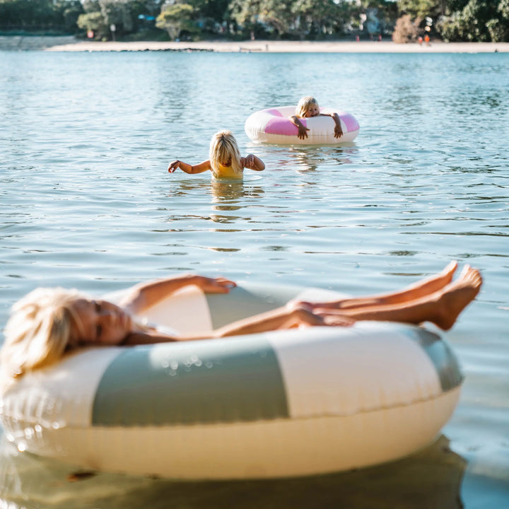 Groen-wit gestreepte zwemband van Sunnylife drijvend op helder water