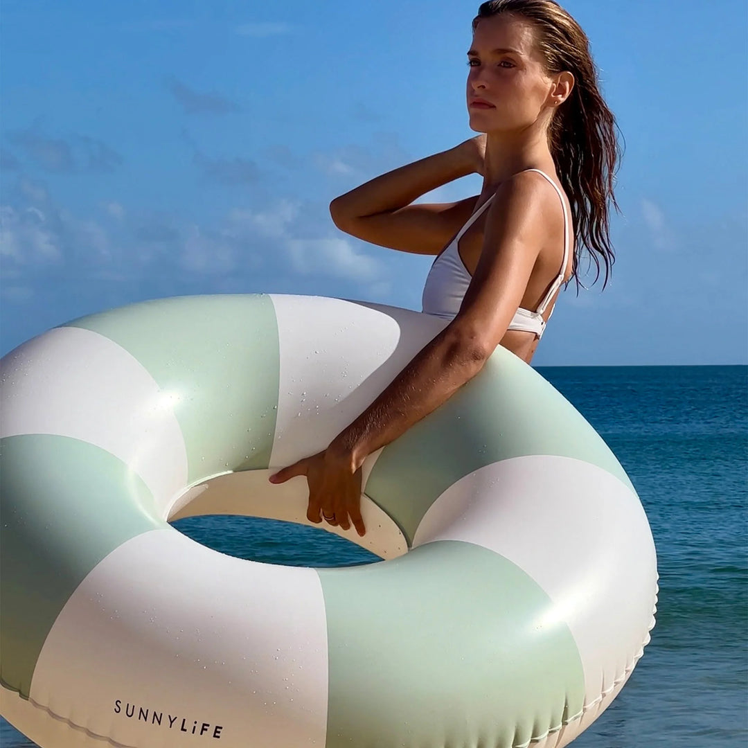 Groen-wit gestreepte zwemband van Sunnylife drijvend op helder water