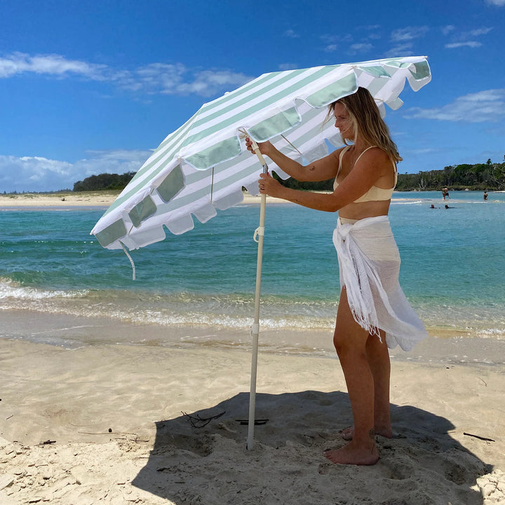 Sunnylife Parasol Compact La Palma in groen-wit gestreept design op het strand