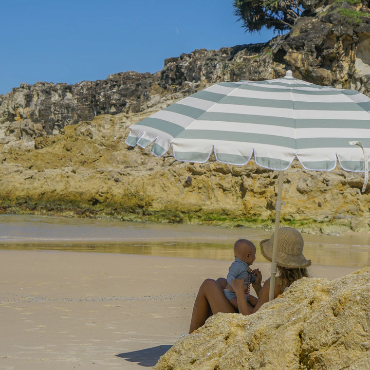 Sunnylife Parasol Compact La Palma in groen-wit gestreept design op het strand