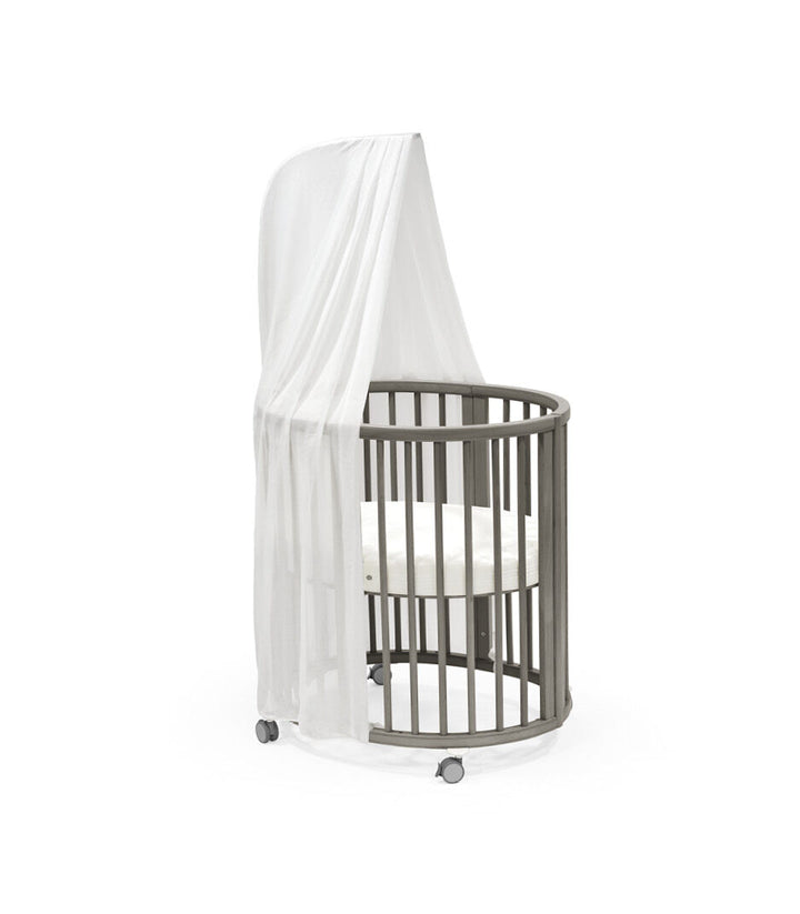 Stokke Sleepi™ Mini V3 wieg in hazy grey afwerking, met zachte ovale vorm en vergrendelbare zwenkwielen.