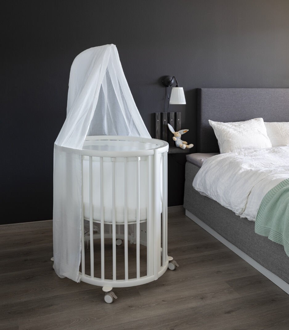 Stokke Sleepi™ Mini V3 wieg in wit, met zachte ovale vorm en vergrendelbare zwenkwielen.