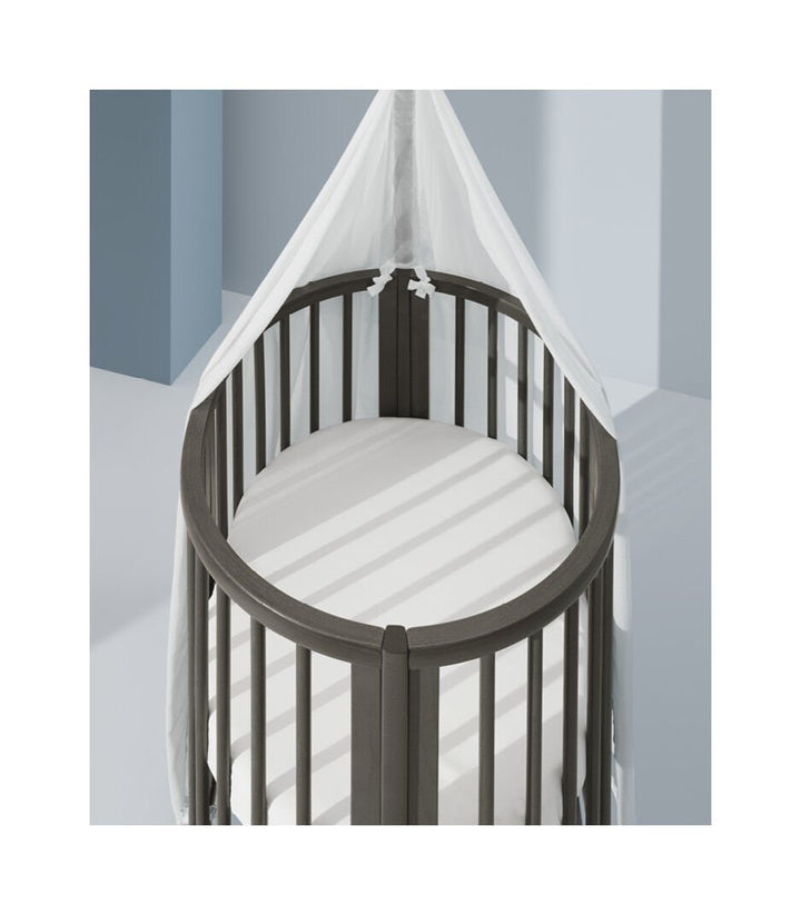 Stokke Sleepi™ Mini V3 wieg in hazy grey afwerking, met zachte ovale vorm en vergrendelbare zwenkwielen.